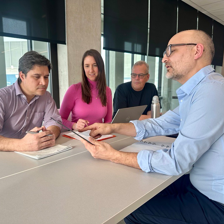 Bright conference room with U-shaped tables and office chairs, large windows showing city views.